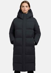 Lang sort dunjakke med høj krave, lynlåslukning og stiklommer. Designet har store syede sektioner for isolering.