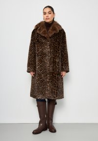 Cappotto di pelliccia leopardato con colletto di pelliccia marrone, con maniche lunghe, taglio dritto e lunghezza media. Abbinato a stivali alti marroni.
