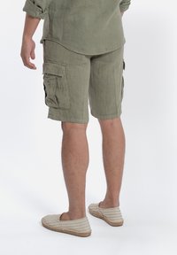 Pantaloni cargo in lino verde oliva con tasche laterali, vestibilità rilassata e orli risvoltati, abbinati a espadrillas a righe.