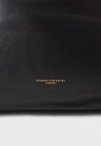Musta nahkainen käsilaukku, jossa on teksturoidu pintaviimeistely ja kullanvärinen kohopainettu "GIANNI CHIARINI FIRENZE" -logo etupuolella.