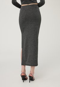 Gonna grigia lunga fino ai piedi con una silhouette aderente, spacco laterale e un sottile motivo testurizzato. Indossata con tacchi neri con accenti di strass.
