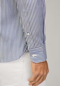 Striped dress shirt in blue and white, featuring a buttoned cuff with a pearl button, tailored fit, and smooth fabric texture.