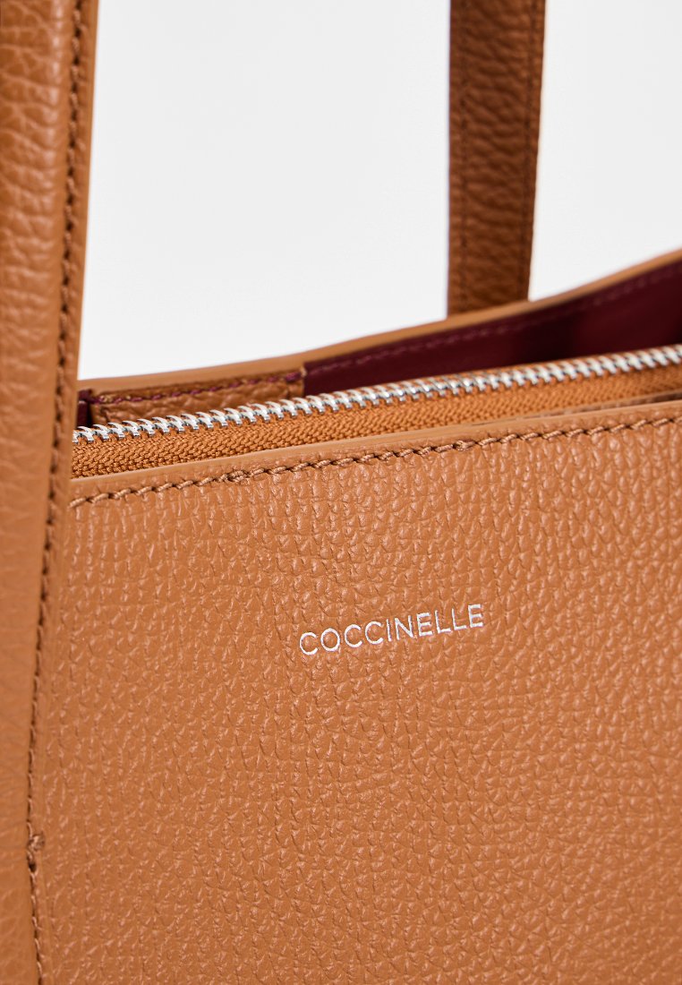 Braune Ledertasche mit strukturierter Oberflächenbeschaffenheit, die ein gefüttertes Fach und ein prägtes Markenlogo in Silber aufweist.