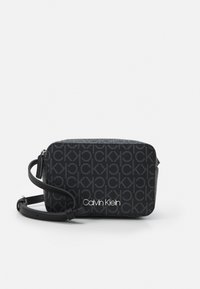 Borsa a tracolla nera di marca con motivo logo testurizzato, dotata di chiusura con zip e tracolla regolabile. Marchio "Calvin Klein" bianco.