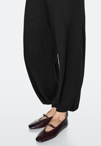 Schwarze, locker sitzende Hose aus weichem Stoff mit zulaufenden Knöcheln, kombiniert mit burgunderfarbenen, krokodilprägemusterten Ballerinas mit einem Riemen über dem Fuß.