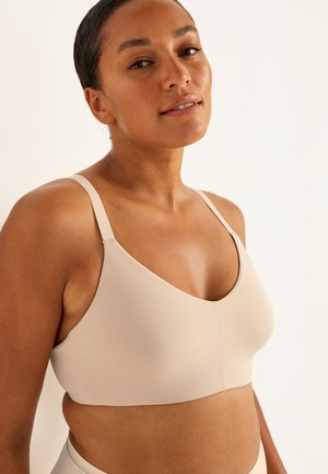 Beige draadloze bh met een diepe decolleté, gemaakt van gladde stof. Het heeft verstelbare bandjes en een naadloze constructie.