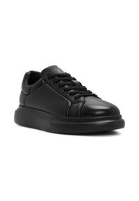 Zapatillas de cuero negro con punta redondeada, cierre de cordones, logo sutil en la lengüeta y una suela de goma gruesa y texturizada.