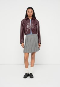 Bordowa krótka kurtka o połyskującej teksturze, zestawiona z plisowaną czarno-białą spódnicą w kratę, białymi skarpetkami do kolan i czarnymi butami.