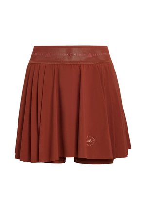 Jupe de tennis plissée couleur rouille avec une large ceinture élastique, des shorts intégrés et un petit logo circulaire Adidas par Stella McCartney près de l'ourlet.
