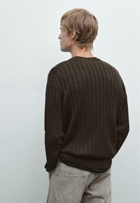 Brun ribbad stickad tröja med långa ärmar, med rund halsringning och texturerad tyg, bärs över grå jeans. Visat ur bakifrån.