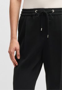 Pantaloni neri dal fit rilassato, con vita elastica, chiusura con cordino e dettagli in metallo color argento.