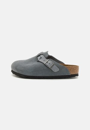 Pilkos suede slip-on klumpės su sagties akcentu ir kamštinės pado, turinčios tekstūruotą paviršių ir juodą gumos padais.