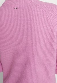 Pull rose en tricot avec texture côtelée. Présente un petit logo métallique à l'arrière de l'encolure. Encolure ronde et coupe décontractée.