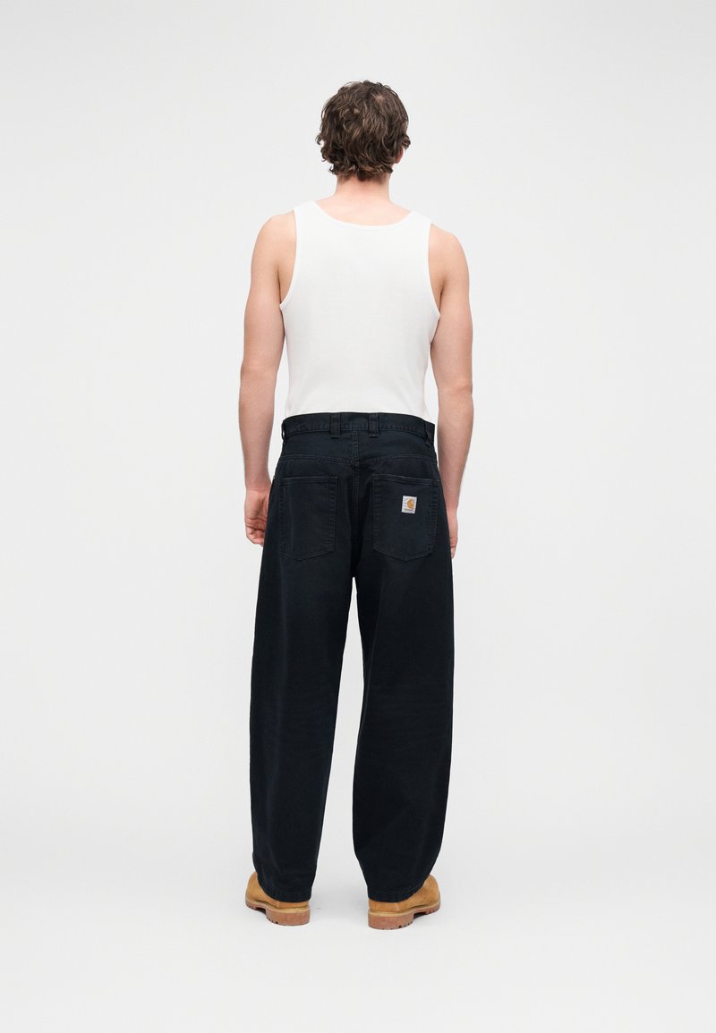 Løse sorte denimbukser med høj talje, udstyret med to baglommer og en tanfarvet læder mærke, båret med en hvid tanktop.