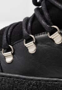 Bota de senderismo negra con ante texturizado, ojales metálicos y cordones. Cuero duradero con una suela texturizada para un mejor agarre.