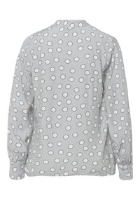 Blouse grise à manches longues avec un motif de cercles contournés en noir, poignets boutonnés et encolure arrondie avec un léger pli à l'arrière.