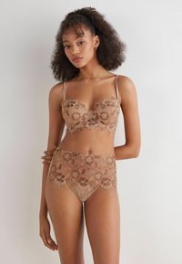 Snygg lacy bralette och högmidjade trosor i nude, med blommönster och vågiga kanter. Genomskinliga band framhäver den skira designen.