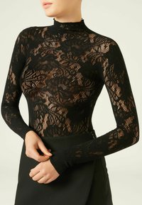 Czarny koronkowy body z długimi rękawami, wysokim kołnierzem, kwiatowym wzorem i dopasowanym krojem, noszony z dopasowaną czarną spódnicą.