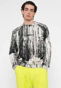 Sort-hvidt trykt sweatshirt med et tekstureret, abstrakt design. Har rund halsudskæring og ribbede ærmeender. Kontrasterer med neongule bukser.