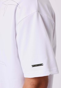 Witte korte mouwen polo met een gladde textuur, voorzien van een subtiel ontwerp op de schouder en een metalen logo-accent op de mouw.