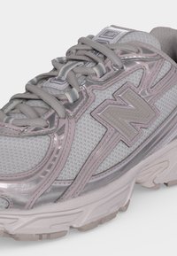 Γκρι και ροζ αθλητικό παπούτσι New Balance με πλέγμα στο πάνω μέρος, χοντρή σόλα και κορδόνια δεμένα χαλαρά σε φιόγκο.