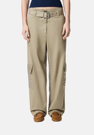 Pantaloni cargo beige con gamba larga, dotati di una vita con cintura, tasche a patta sui lati e una consistenza morbida. Abbinati a pantofole mocassino marroni.