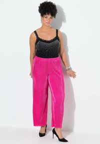 Top negro sin mangas con borde de encaje y adornos de piedras brillantes, combinado con pantalones anchos plisados de color rosa vibrante, usados con tacones negros.