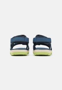 Blå nylon-sandaler med justerbara remmar, vadderad sula och en hållbar, texturerad grön gummisula. Bakifrån visar de remdesignen.
