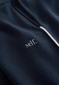 Sweat-shirt marine avec texture douce, équipé d'un cordon blanc et du logo "self." brodé. Design simple et minimaliste.