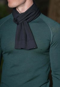 Écharpe tricotée gris foncé drapée sur un pull vert ajusté, présentant une texture lisse et de subtils détails de couture au niveau du col.