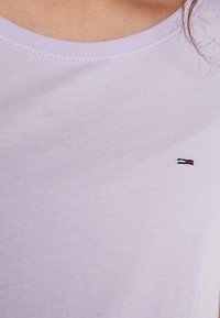 Camiseta de algodón lila claro con cuello redondo y un pequeño logo bordado en colores rojo, blanco y azul en el pecho.