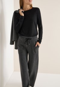 Top negro de manga larga combinado con pantalones grises que cuentan con bolsillos laterales y una cintura con cordón. Tejido suave con un ajuste cómodo.