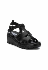 Sandalias de cuña negras con correas anchas entrelazadas, hebilla ajustable en el tobillo y suela texturizada. Fabricadas con materiales sintéticos.