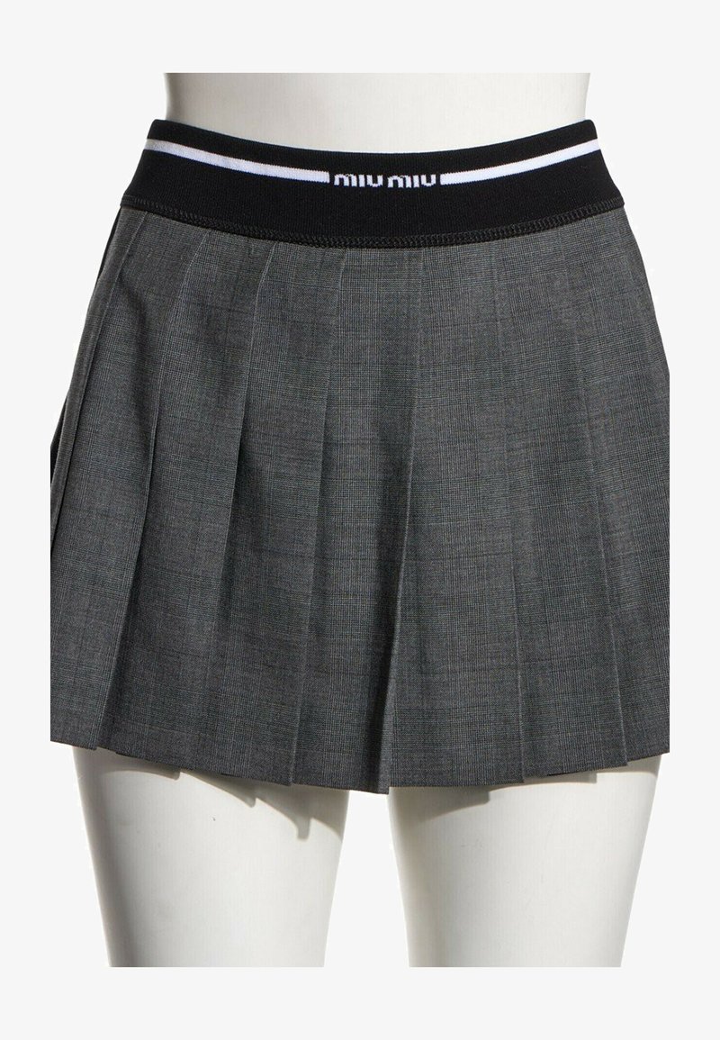 Jupe plissée gris foncé avec taille élastique noire comportant des bandes blanches et un texte partiel de logo blanc sur un mannequin.