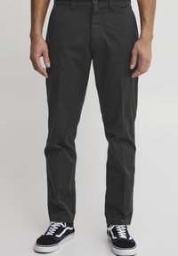 Black cotton trousers with a straight-leg fit, featuring a side pocket, front button closure, and worn with black and white sneakers.