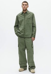 Grön cargoshirt med en bröstficka, kombinerad med vida gröna cargobyxor med sidfickor och stadiga sömmar.