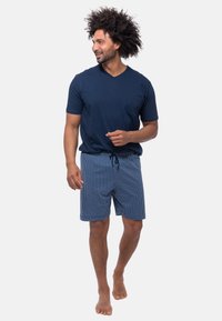 Marine v-hals t-shirt en blauwe geruite zwembroek met koord. Lichtgewicht stof, relaxte pasvorm, korte mouwen, blote voeten.