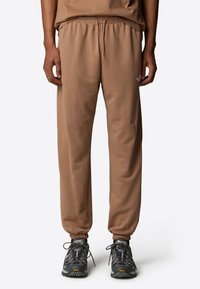Bruine sweatpants met een elastische tailleband en boordjes bij de enkels, gemaakt van zacht materiaal, in combinatie met lichte, textuurrijke sneakers.