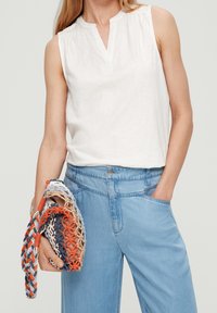White sleeveless top with a V-neck, paired with light blue wide-leg jeans. Handheld multicolored woven bag featuring blue, orange, and beige accents.