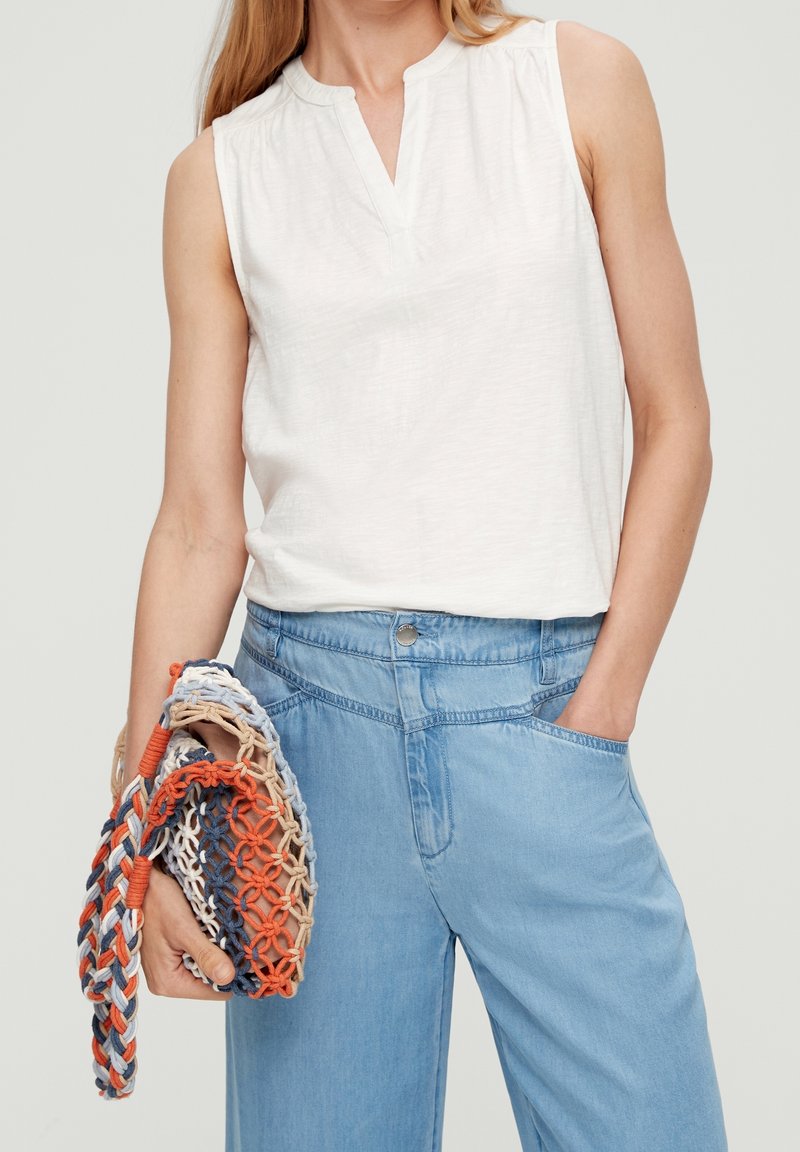 White sleeveless top with a V-neck, paired with light blue wide-leg jeans. Handheld multicolored woven bag featuring blue, orange, and beige accents.