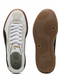 Baskets blanches et noires avec une semelle en caoutchouc texturé, des accents en daim, un système de laçage et un détail en or sur le côté.