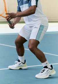 Witte en lichtblauwe sportoutfit met shorts en een T-shirt met ronde hals, gecombineerd met witte sneakers met een groene accente, op een tennisbaan.