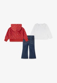 Sweatshirt rouge à capuche avec imprimé floral blanc, haut blanc à manches longues avec fermeture par boutons au dos, et jeans évasés bleu foncé.