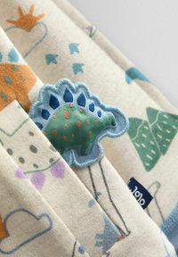 Bavlnená látka s farebnými vzormi dinosaurov a rastlín. Vyšívaná zelená dinosauria aplikácia s modrými a hnedými akcentmi. Textúrovaný, mäkký povrch.