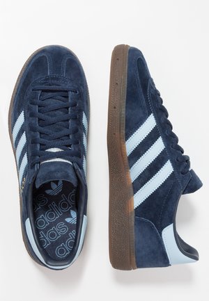 Paire de baskets Adidas en daim bleu foncé avec des bandes bleu clair, semelles en caoutchouc marron et logo Adidas sur les semelles intérieures, vues de dessus et de côté.