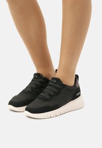 Zapatillas negras con un upper de tela texturizada, diseño de cordones y una suela de goma blanca con un patrón acanalado. Con detalles de logotipo.