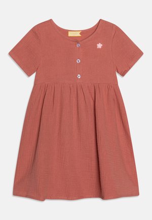 Kūdikiui skirta trumpomis rankovėmis rūdžių raudonos spalvos suknelė su apvalia iškirpte, trimis priekiniais mygtukais, raukšlėtu juosmeniu ir mažu rožiniu žvaigždės užrašu ant krūtinės.