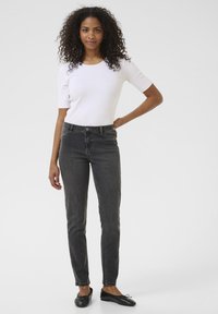 Jean skinny en denim noir avec une taille haute et une légère décoloration, associé à un haut ajusté à manches courtes blanc. Des ballerines noires simples complètent le look.