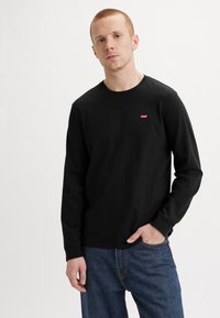 Black long-sleeve t-shirt made of cotton with a round neck. Features a small red Levi's logo on the chest. Worn with blue jeans.