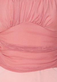 Top rosa con una textura recogida, que presenta un diseño arrugado y un tejido suave. El sujeto está estructurado con un material blando y elástico.